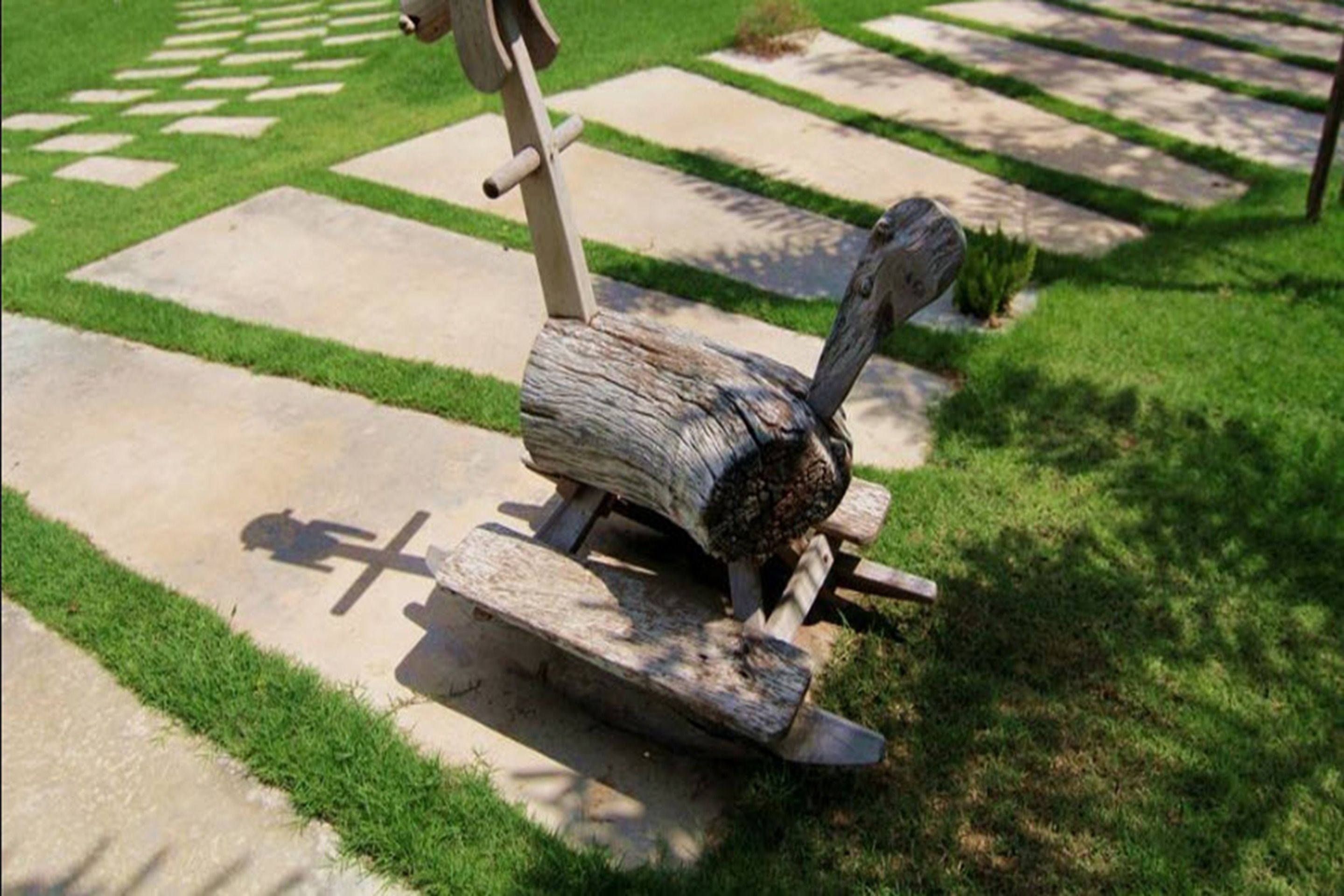 A wooden sculpture of a bird on a stone pathway with grass on either side.