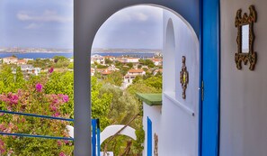 A view from a balcony with a clear sky, a coastal town in the background, and a blue door with a decorative mirror. - Pasalimani Hotel (Cesme)