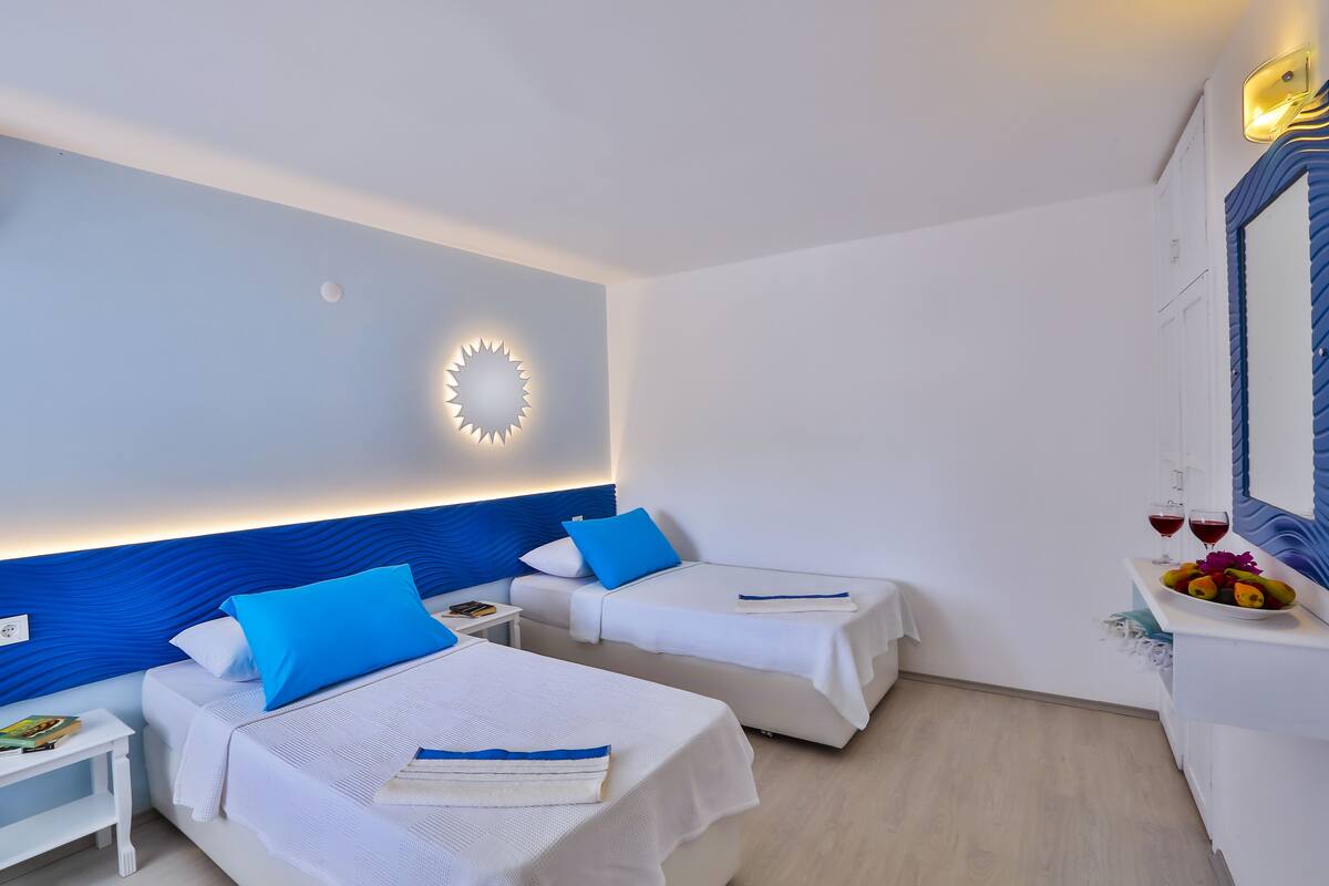 A hotel room with two beds, a nightstand, a wall-mounted light, and a fruit bowl on a counter.
