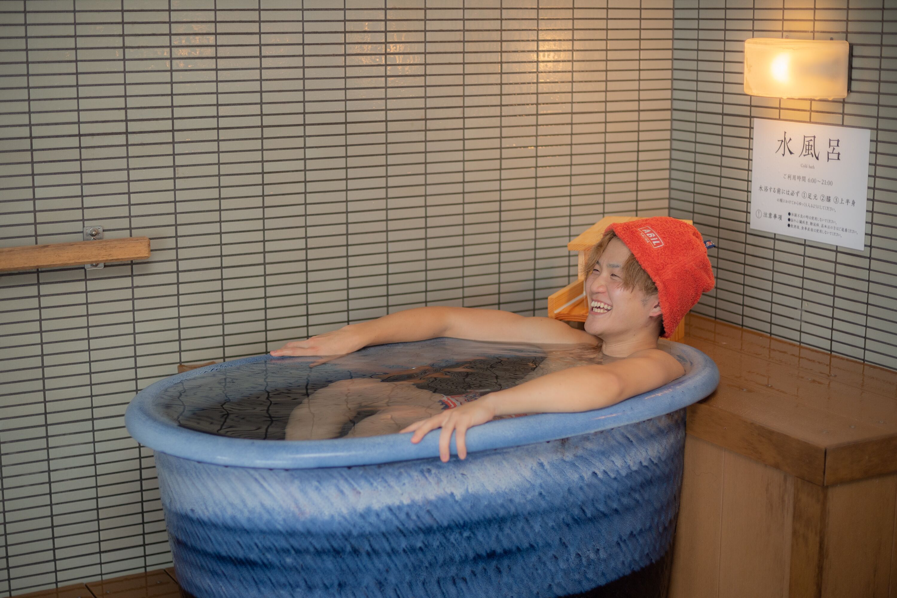A person relaxing in a blue hot tub with a wooden shelf and a sign in the background.