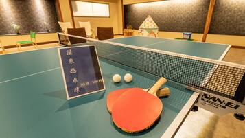 A ping pong table with two paddles and two balls, a sign with pricing, and a small house decoration.