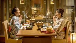 Two people seated at a table with traditional Japanese dishes, in a room with glass walls and a modern interior.