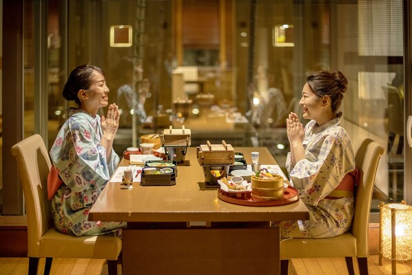 Dos personas sentadas en una mesa con platos tradicionales japoneses, en una habitación con paredes de vidrio y una decoración moderna.