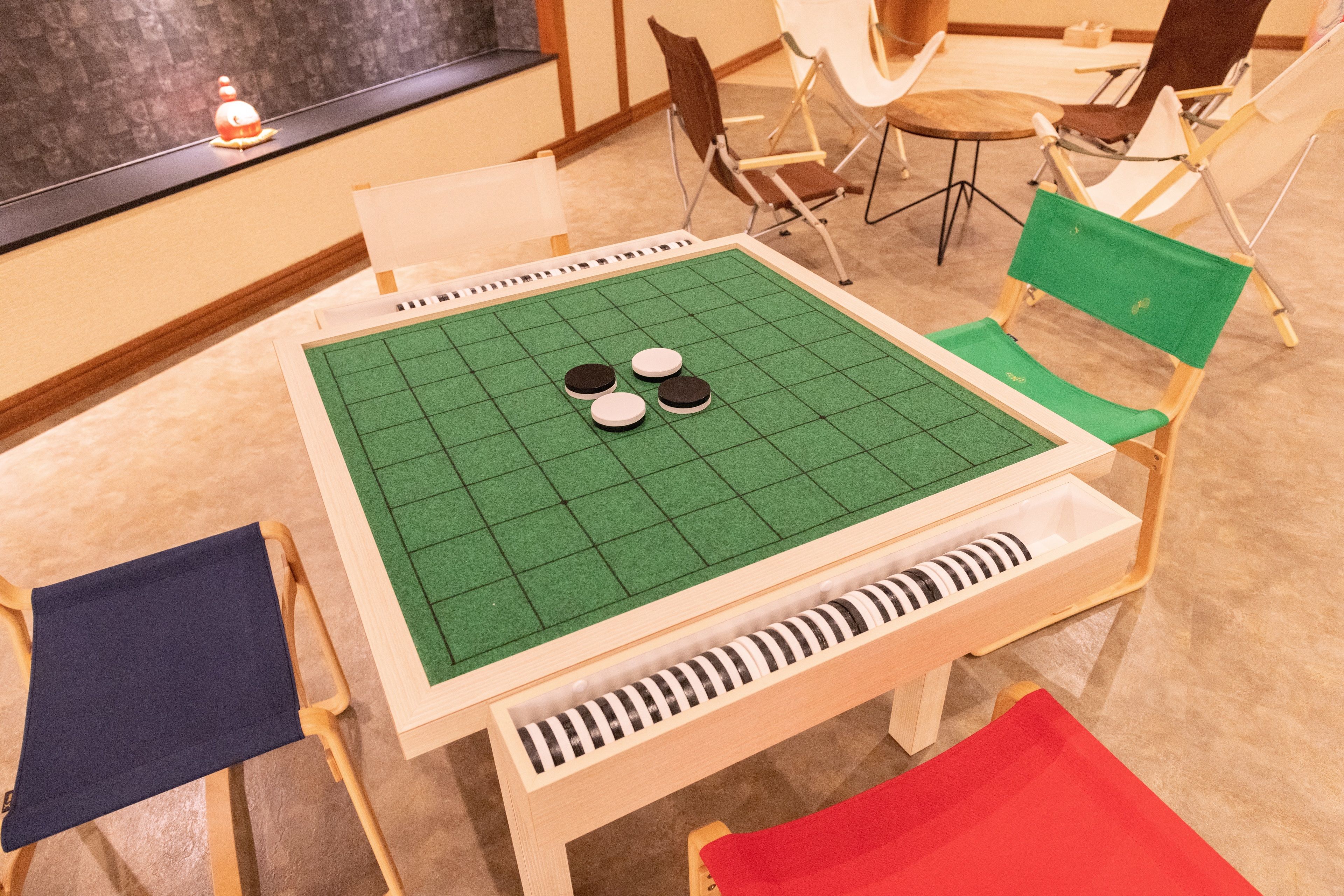 A Go board with four stones on a green felt surface, surrounded by folding chairs and a small table.