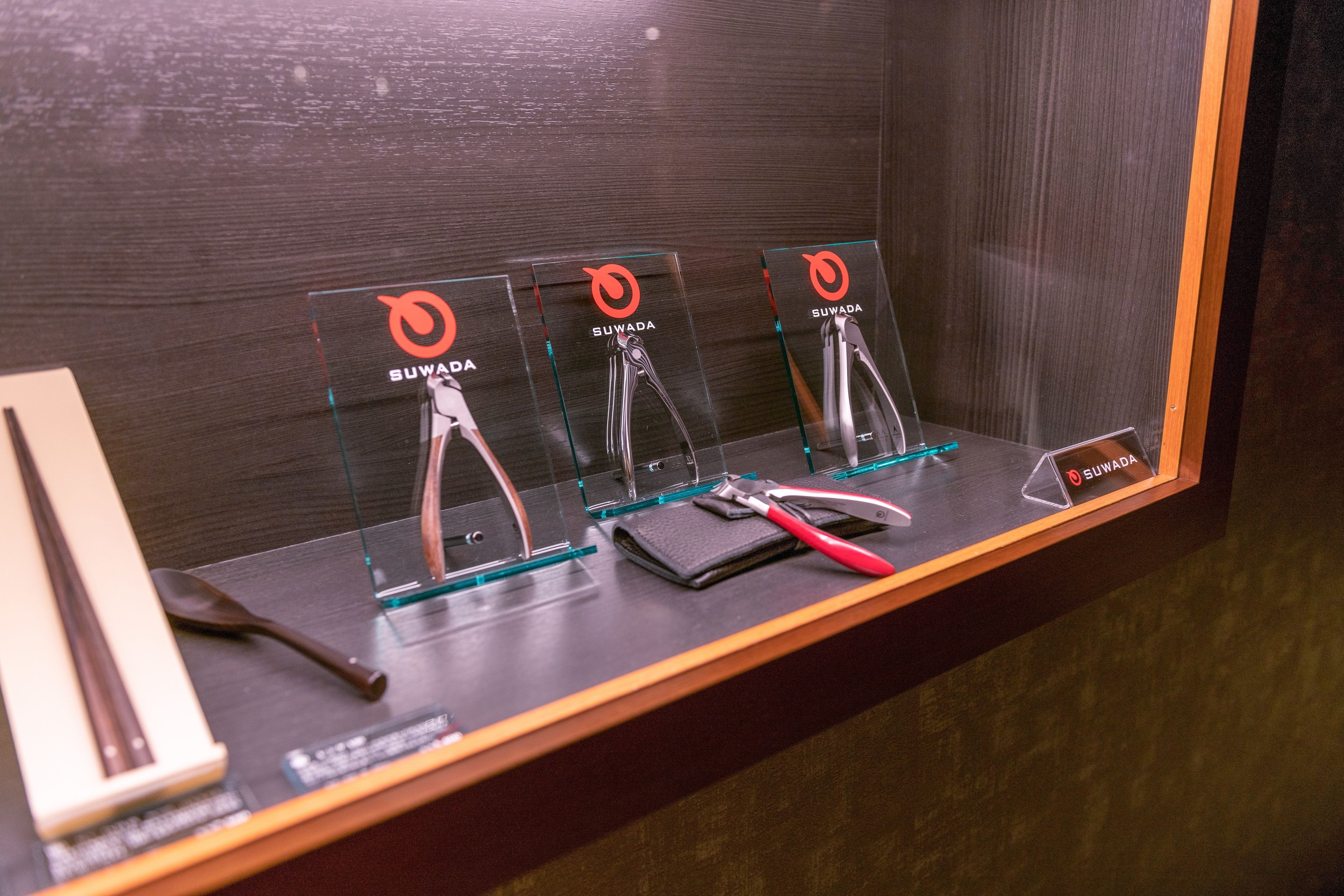 A display of Suwada branded tools in a glass case, with a wooden frame and a dark background.