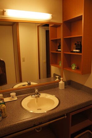 Un baño con lavamanos, espejo y repisas con artículos de aseo.