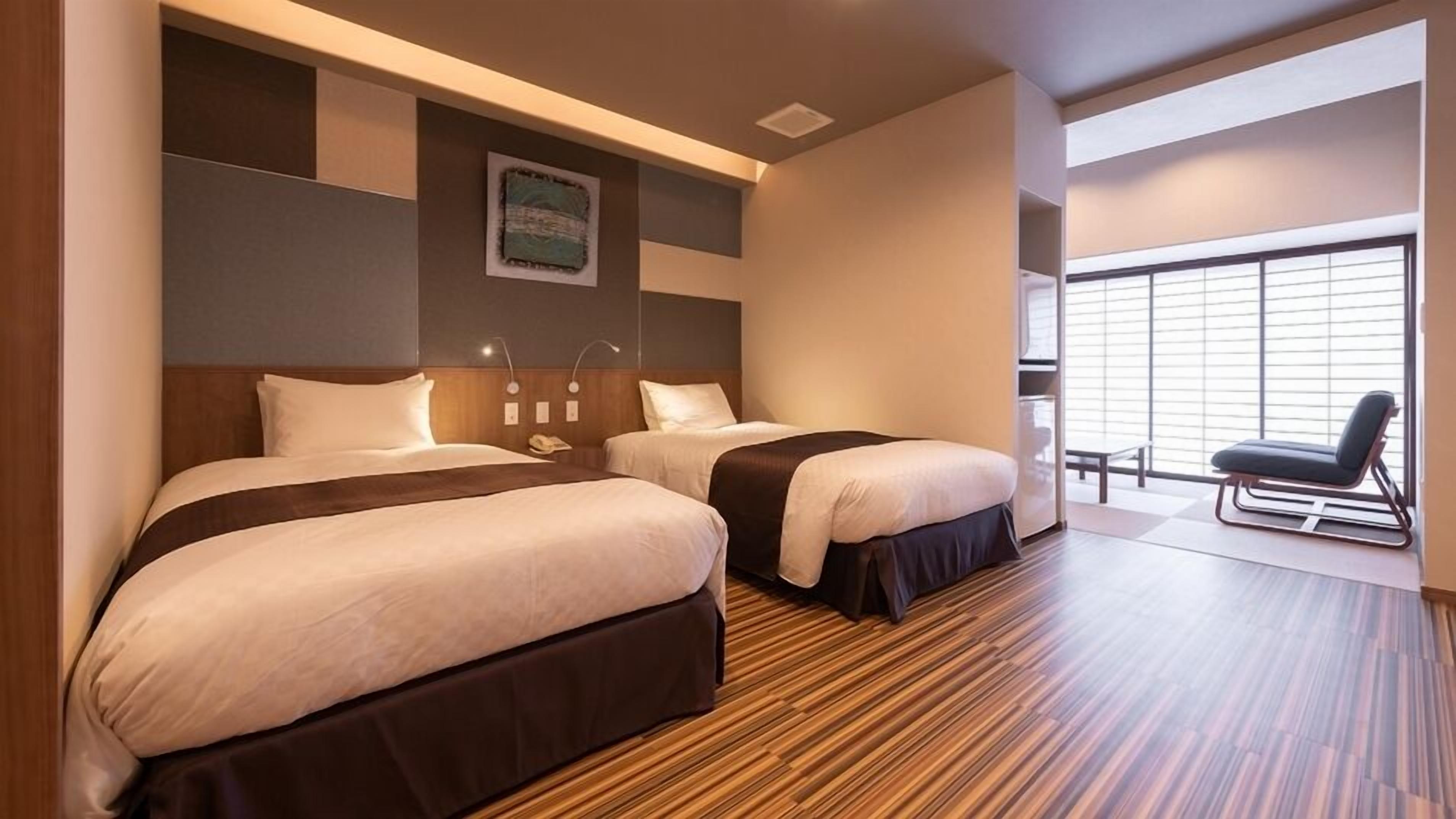 Habitación de hotel con dos camas, piso de madera, un ventanal grande con persianas y una silla junto a la ventana.
