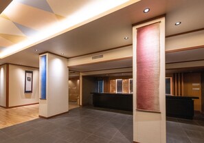 Un vestíbulo de hotel con un mostrador de recepción, un pilar grande y un cuadro en la pared.
