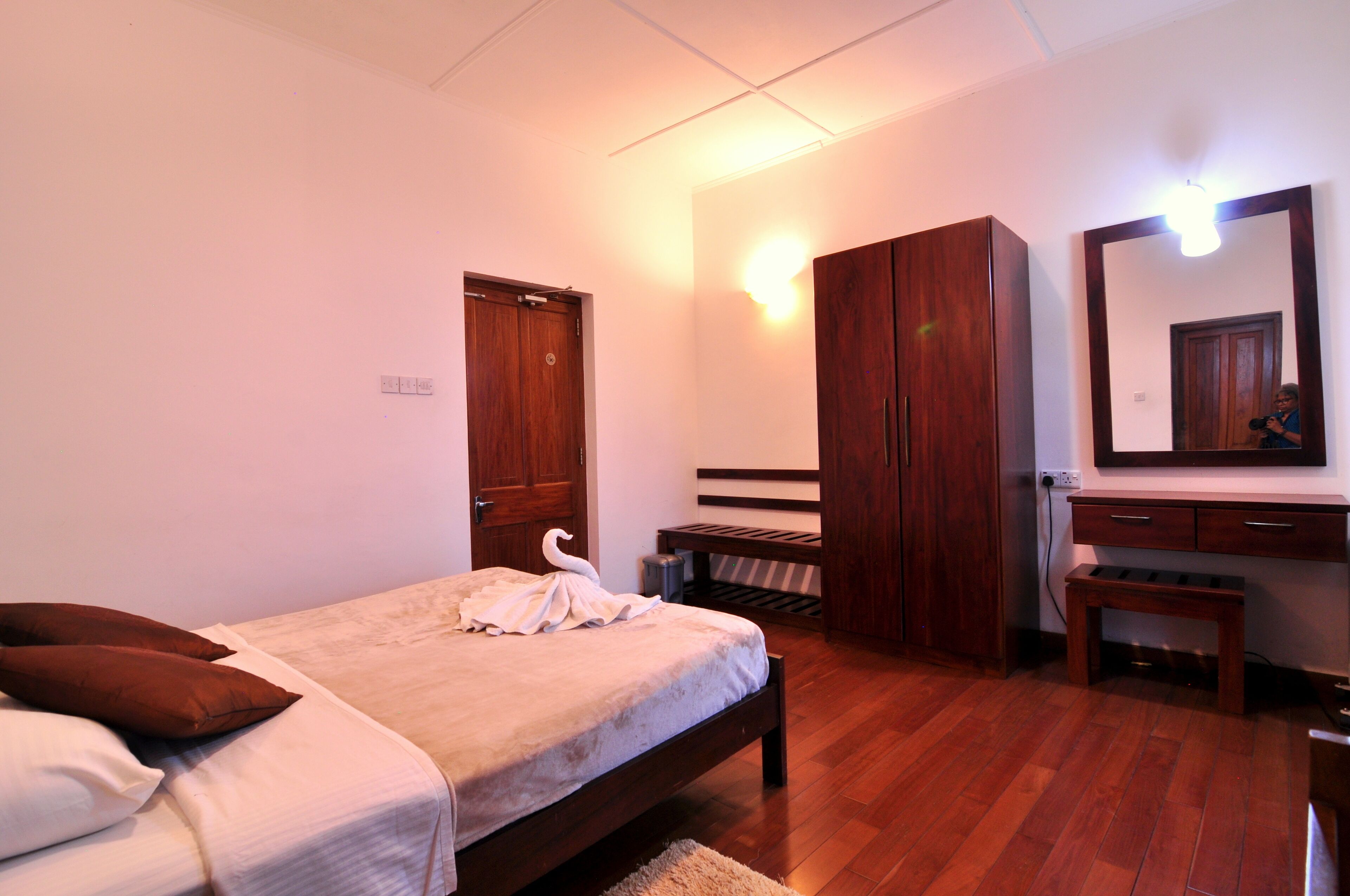 A bedroom with a bed, wooden wardrobe, a mirror, and a bench.