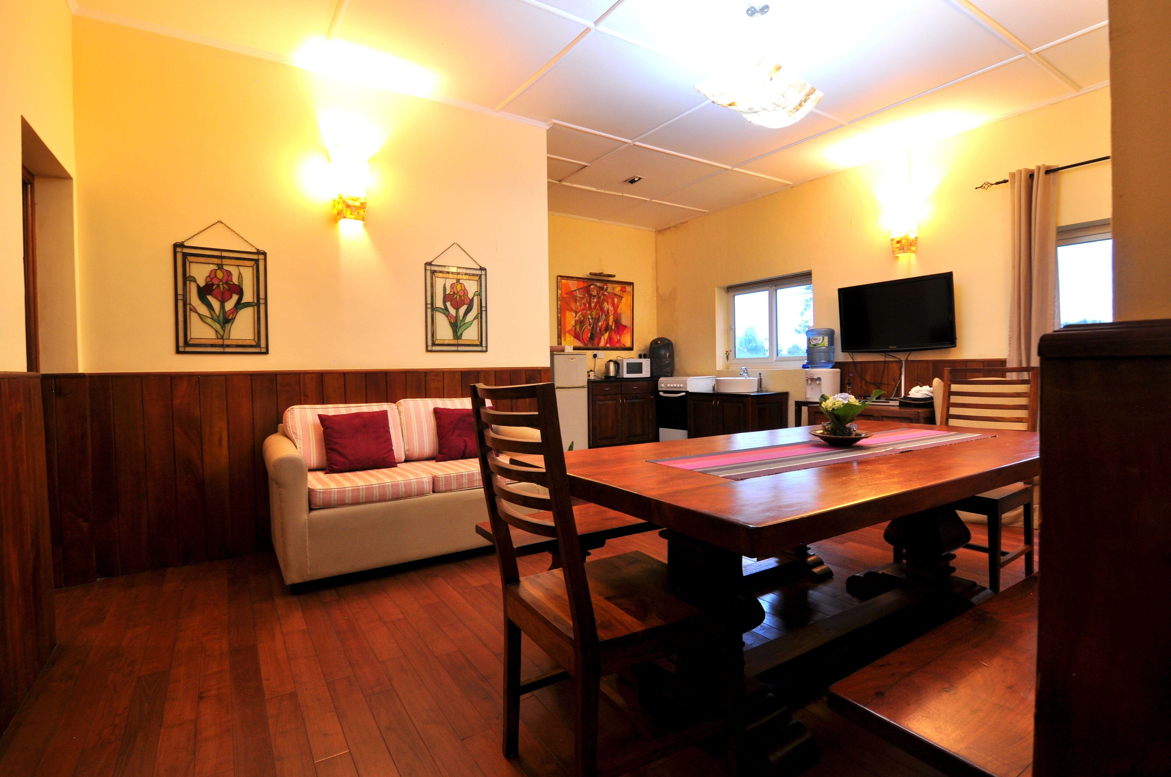 A dining area with a wooden table and chairs, a sofa with cushions, a television, and artwork on the walls.