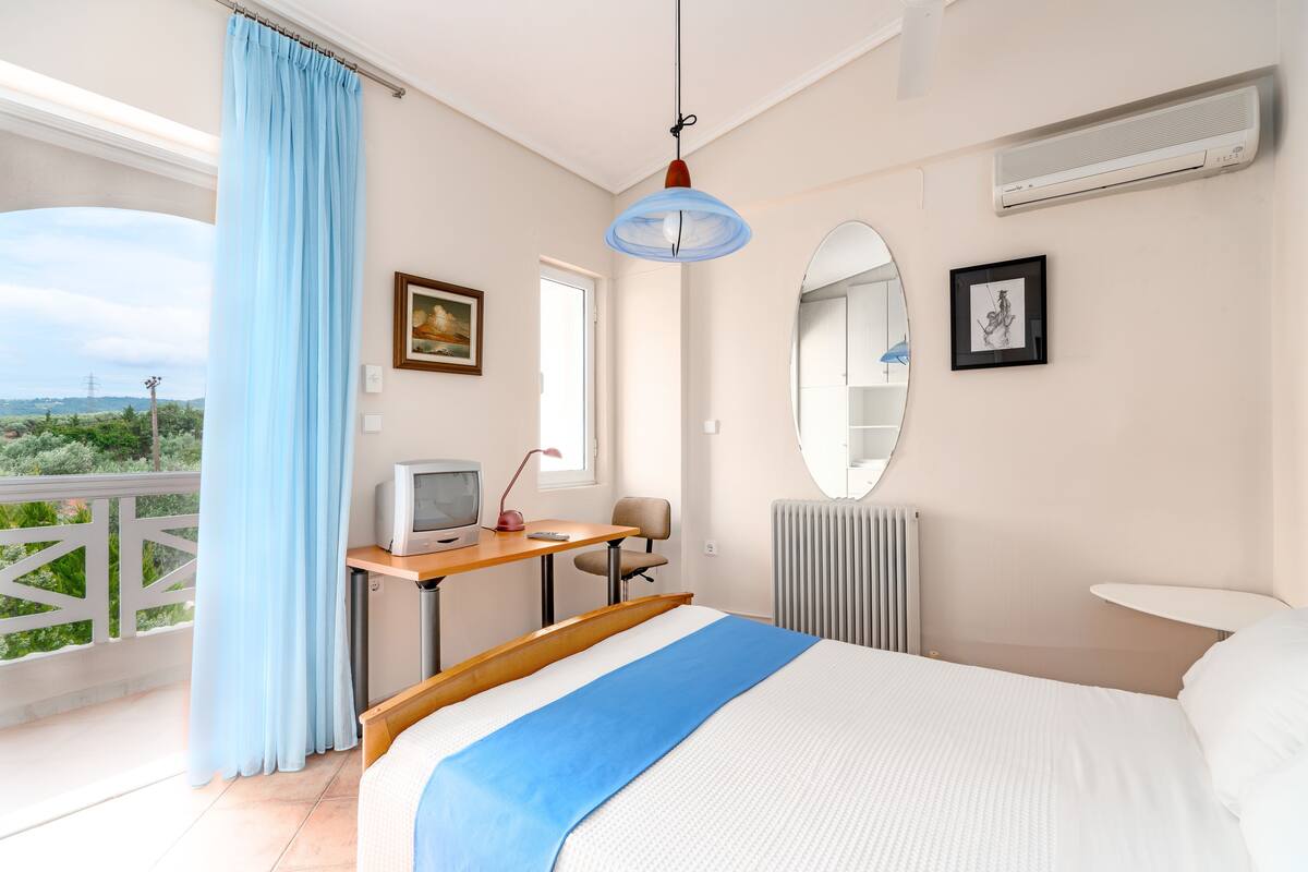 Ein Schlafzimmer mit einem Bett, einem Schreibtisch mit Computer, einem Fernseher und einem Fenster mit Blick.
