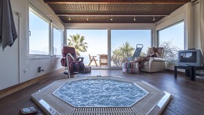 A spacious room with a large octagonal hot tub, wooden flooring, and a view of the ocean through large windows.