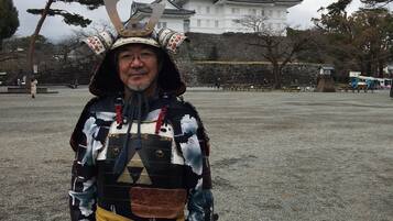 A person in traditional samurai attire standing in front of a castle.