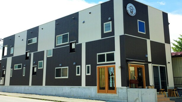 A modern multi-story building with a dark facade, multiple windows, and a visible entrance with a door.