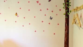 A bedroom with a wooden bed, a wall decorated with pink flowers and butterflies, and a wooden tree trunk.