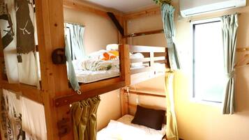 A bunk bed room with wooden walls, a window with curtains, and a bed with a floral bedspread.