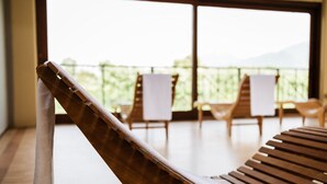 Uma cadeira de lounge de madeira com uma toalha branca, uma mesa de madeira e vista para uma varanda com cadeiras e toalha de mesa branca.