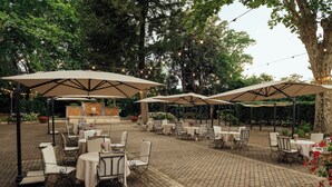 Um terraço ao ar livre com mesas e cadeiras, cercado por árvores e luzes de Natal.