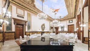 Uma grande sala de baile com um piano de cauda Steinberg preto imponente, lustres ornamentados e mesas decoradas com louças brancas.