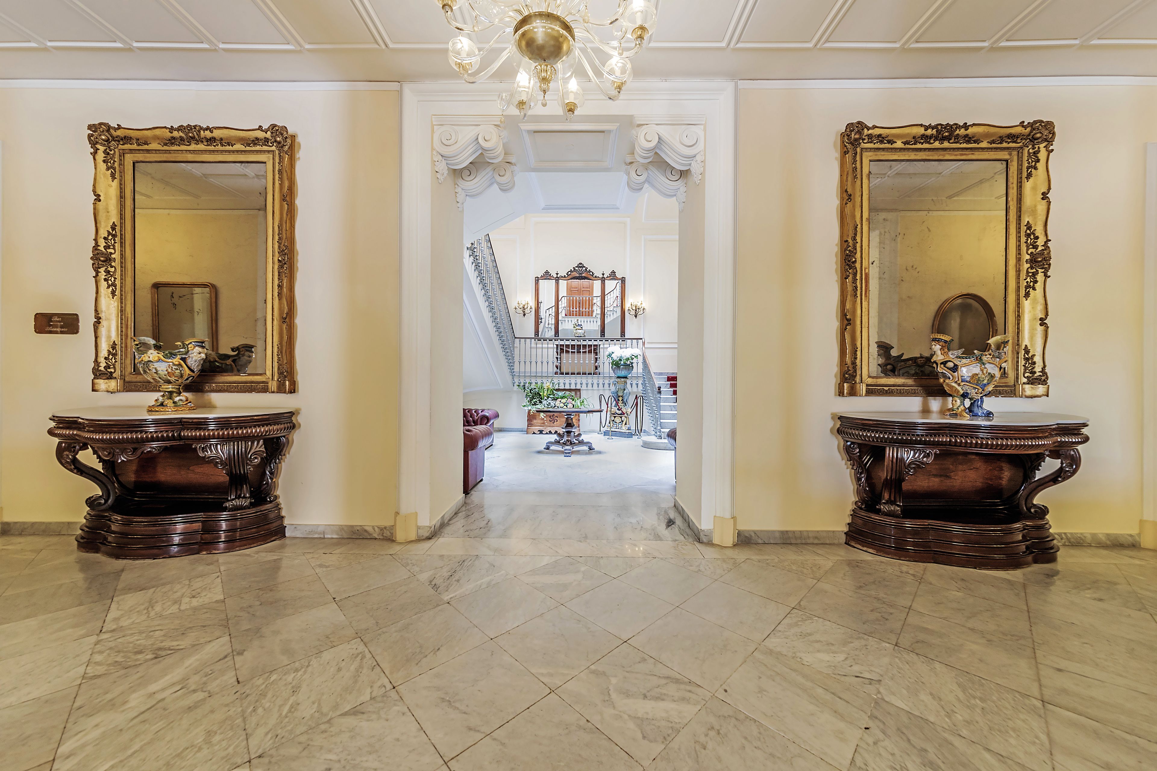A grand hallway with marble flooring, ornate wooden furniture, and large mirrors on either side.