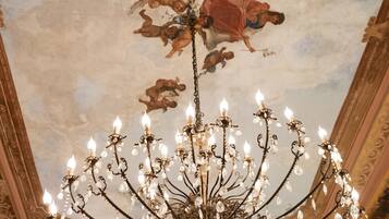 A grand chandelier with multiple arms and crystal decorations, set against a ceiling with painted clouds and cherubs.