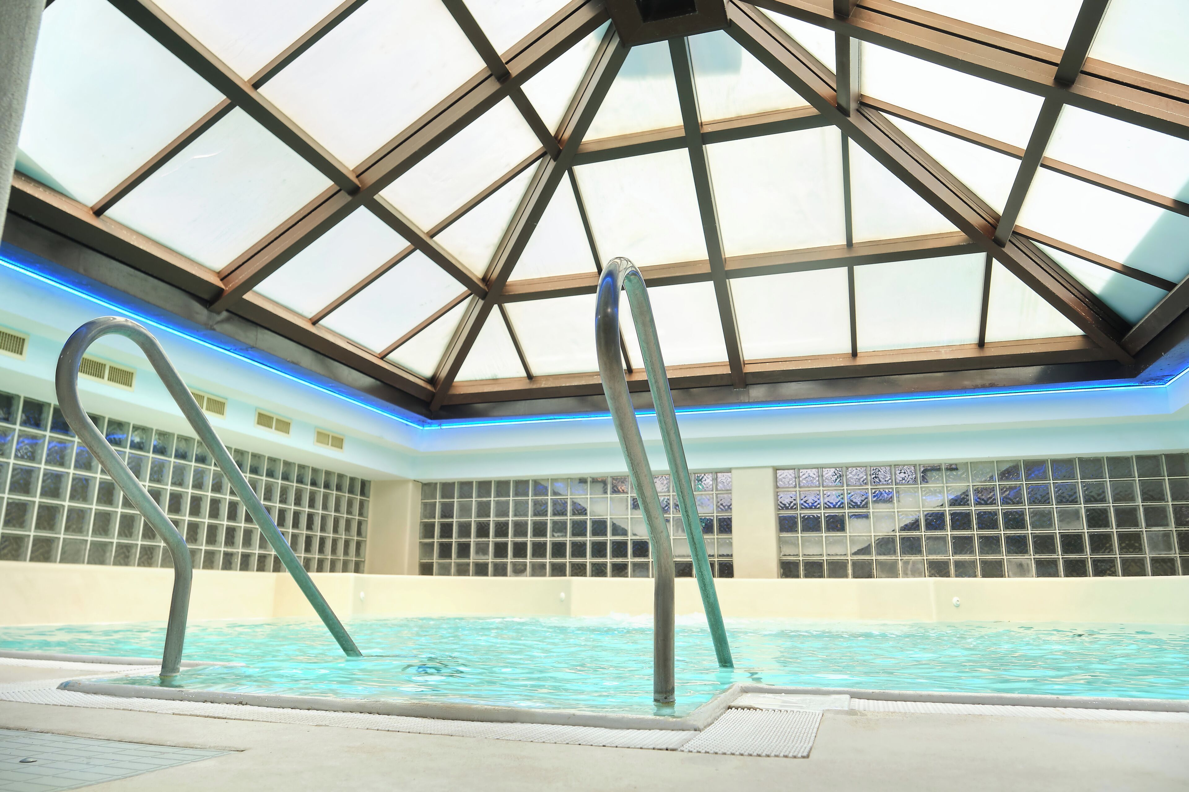 Una piscina interior con techo de cristal y escaleras de metal.