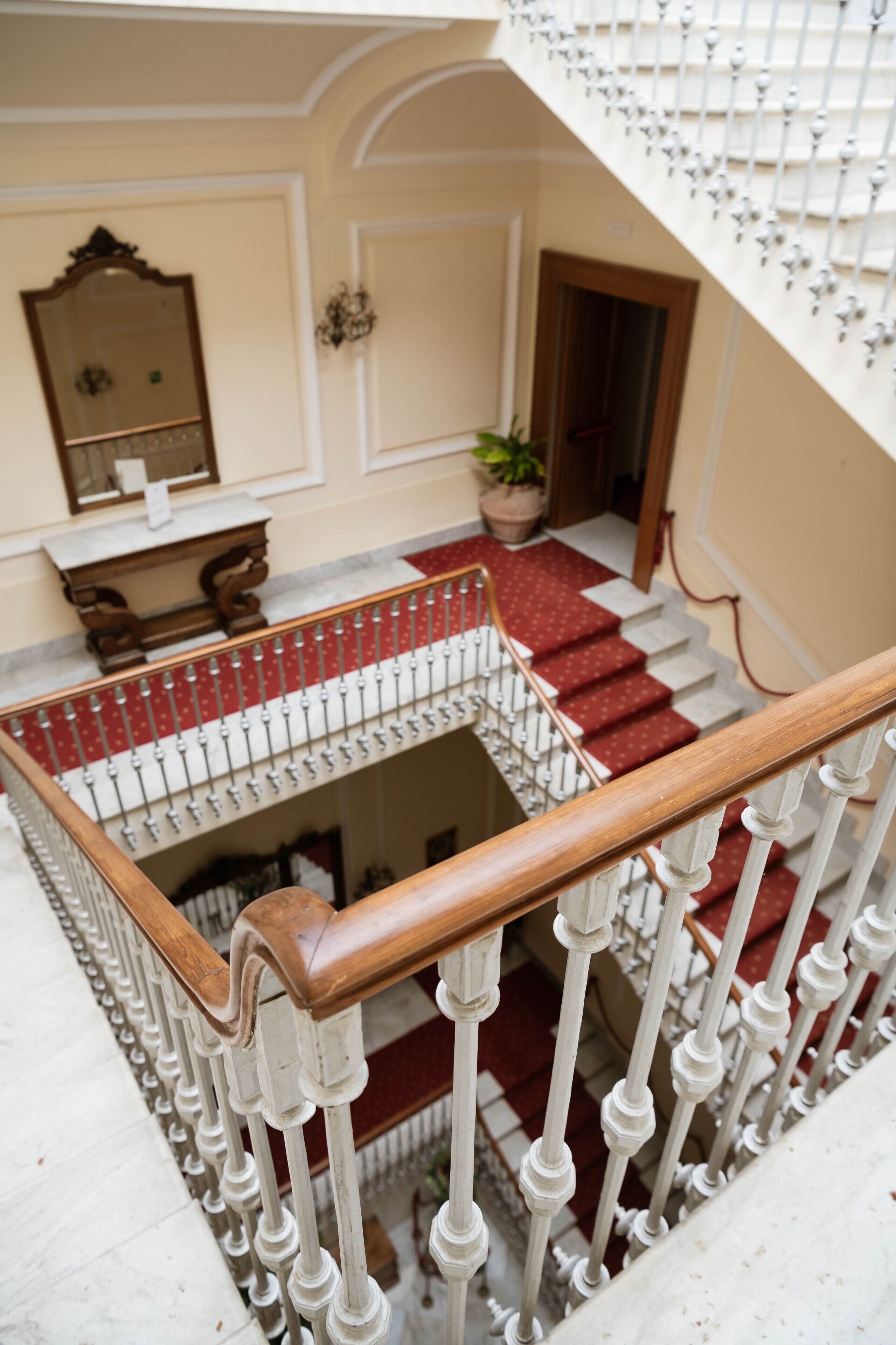 A staircase with white balusters and a red carpet, leading to a lower level.