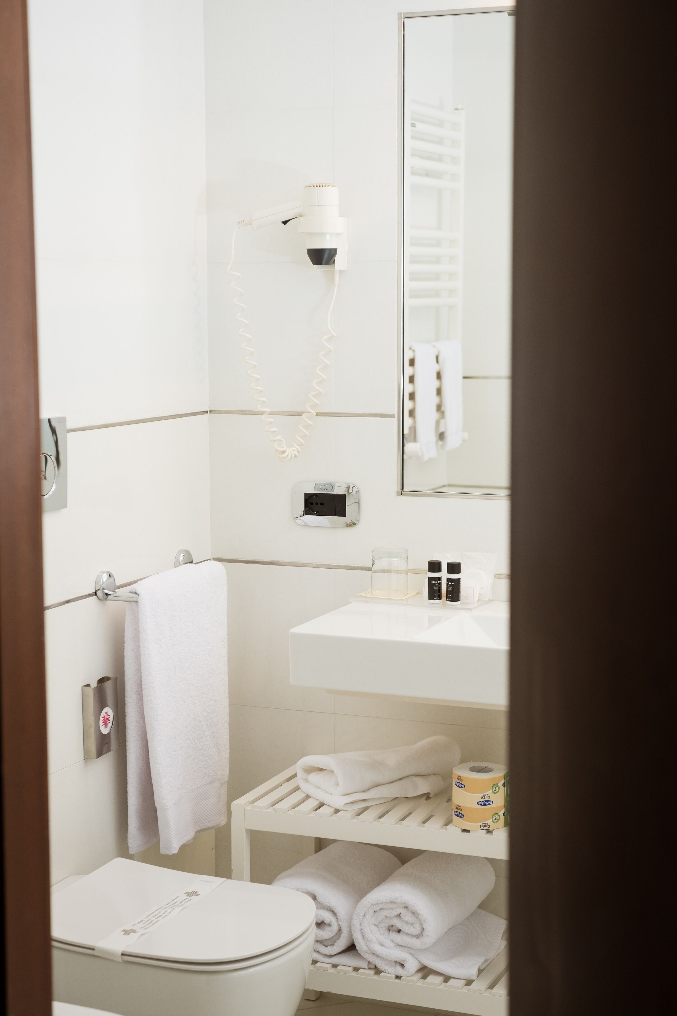 Un baño con inodoro, lavamanos, espejo y toallero.