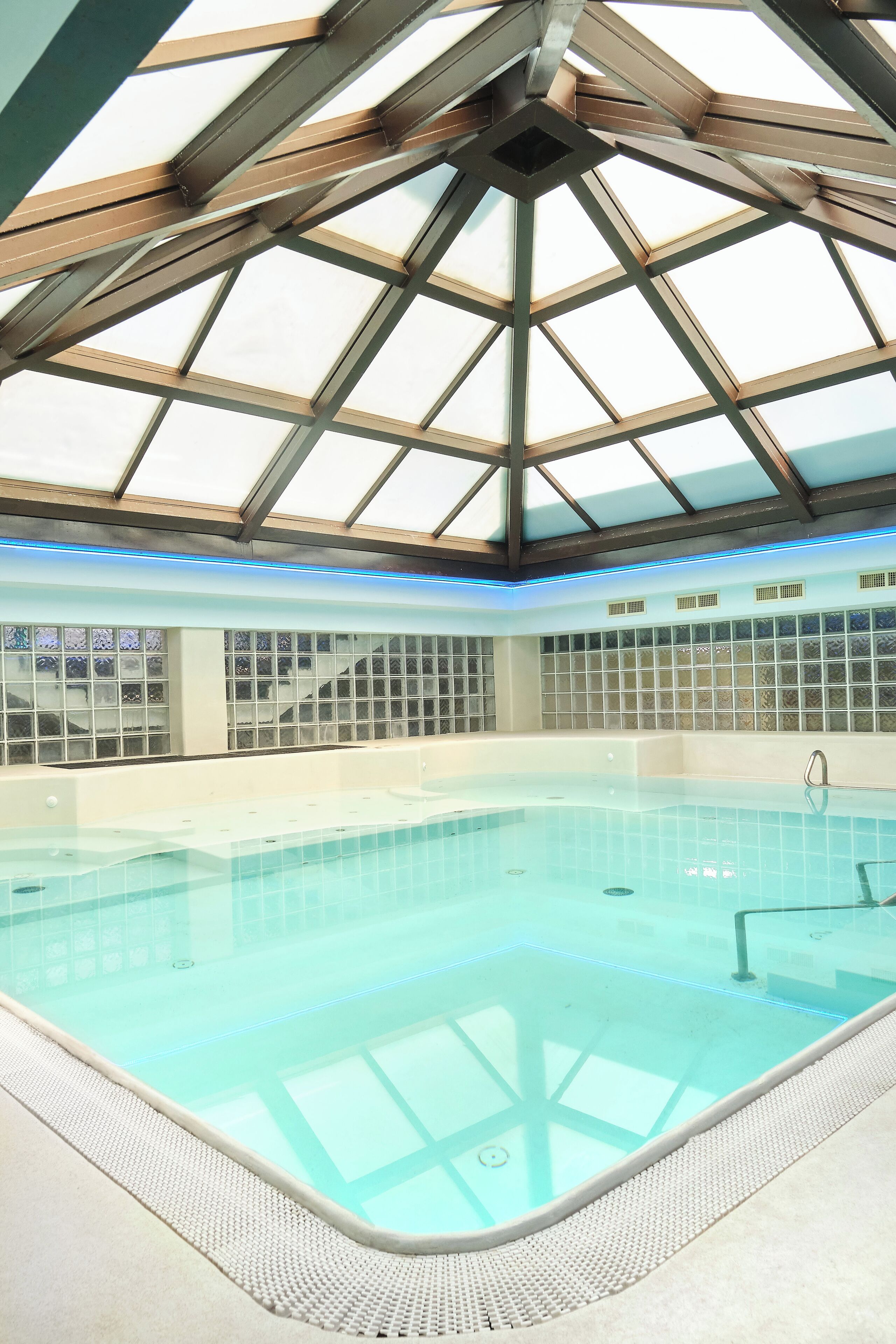 Une piscine intérieure dotée d’un toit en verre et d’un mur recouvert de carreaux.