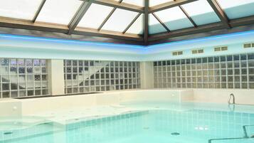Une piscine intérieure dotée d’un toit en verre et d’un mur recouvert de carreaux.