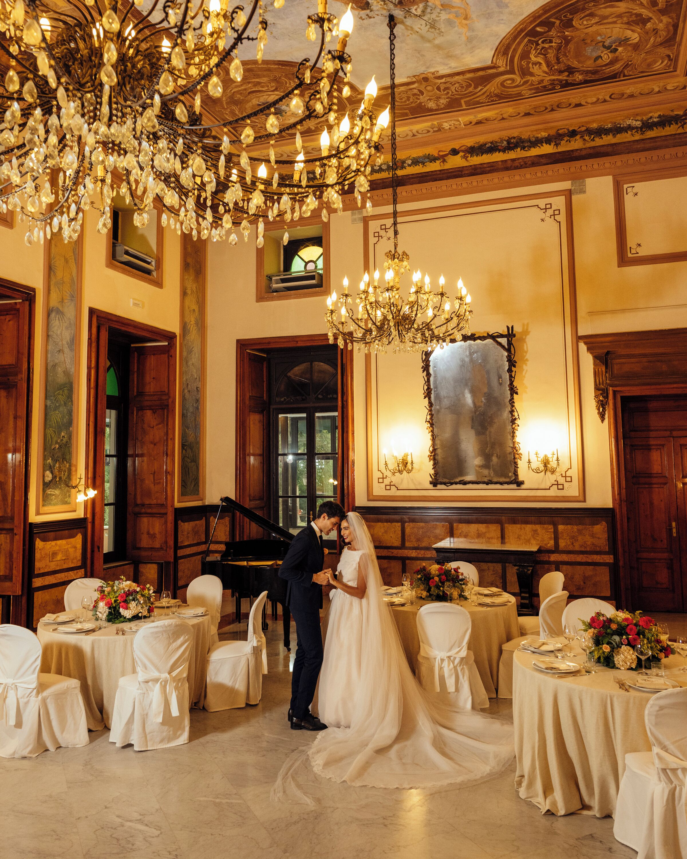 A wedding reception with a grand chandelier, a piano, and ornate wall decorations.