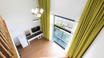 A modern apartment with a balcony, a TV, a small desk, and a hanging light fixture.