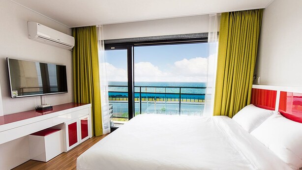 Une chambre d’hôtel avec un grand lit, une télévision, un bureau et un balcon offrant une vue sur l’océan.