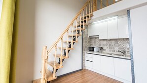 Un escalier menant à une cuisine avec des meubles blancs et un four à micro-ondes.