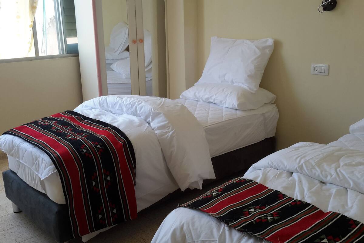 Quarto de hotel com duas camas, uma janela com cortinas, um espelho e uma tomada na parede.