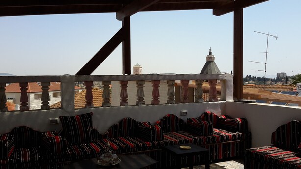 A balcony with striped sofas and a table, overlooking a cityscape with buildings and a tower. - Daher Guest House Nazareth - Hostel (Nazareth)