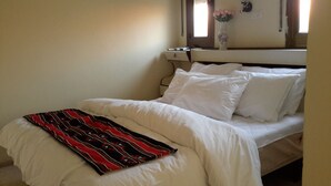 A bed with white bedding and a red and black blanket, a vase with flowers on the nightstand, and a window with curtains. - Daher Guest House Nazareth - Hostel (Nazareth)