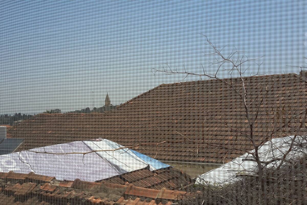 Um edifício amplo com telhado plano e padrão em grade, cercado por árvores e céu claro.