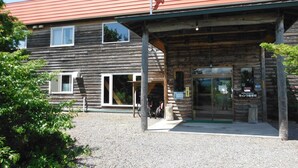 A rustic wooden building with a red roof, a covered entrance, and a gravel driveway. - Clione Camp Guest House (Shari)
