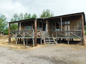 A rustic wooden building with a porch and a staircase leading to a second level.