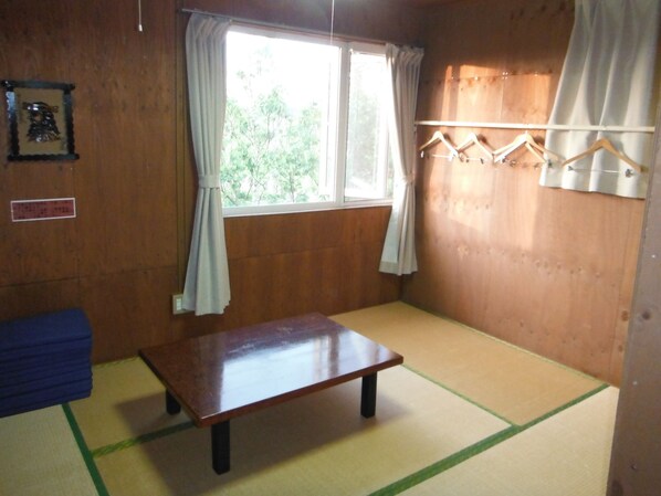 A room with a wooden floor, a small wooden table, a window with curtains, a blue sofa, and a coat rack with hangers.