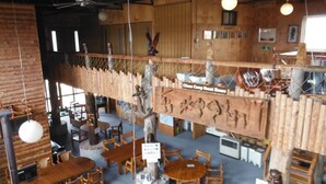 A rustic wooden interior with multiple dining tables and chairs, a wooden climbing wall, and a sign indicating a guest house. - Clione Camp Guest House (Shari)