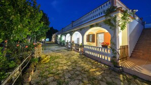 A courtyard with a stone floor, a wooden fence, and a building with arched windows and a balcony. - La Formichina (Peschici)