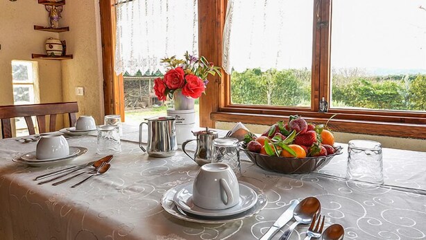 A dining table set with plates, cups, cutlery, a pitcher, and a bowl of fruit, with a window view of greenery. - La Formichina (Peschici)