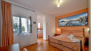 A bedroom with a bed, a painting, a window with curtains, and a door. - La Formichina (Peschici)