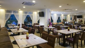 A restaurant with multiple dining tables and chairs, a sofa area, and large windows with sheer curtains. - One Pacific Hotel & Serviced Apartments (George Town)