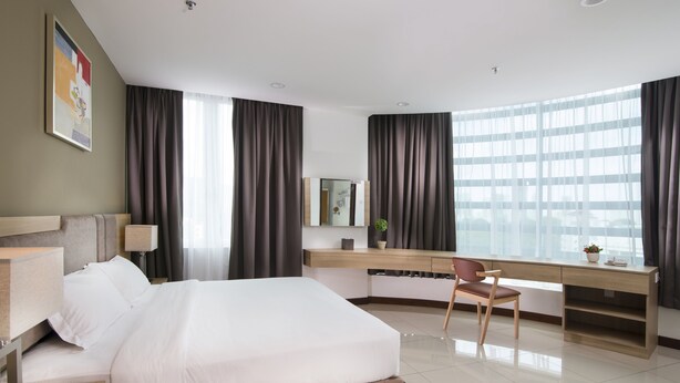A modern hotel room with a large bed, a desk with a chair, a mirror, and a window with curtains. - One Pacific Hotel & Serviced Apartments (George Town)