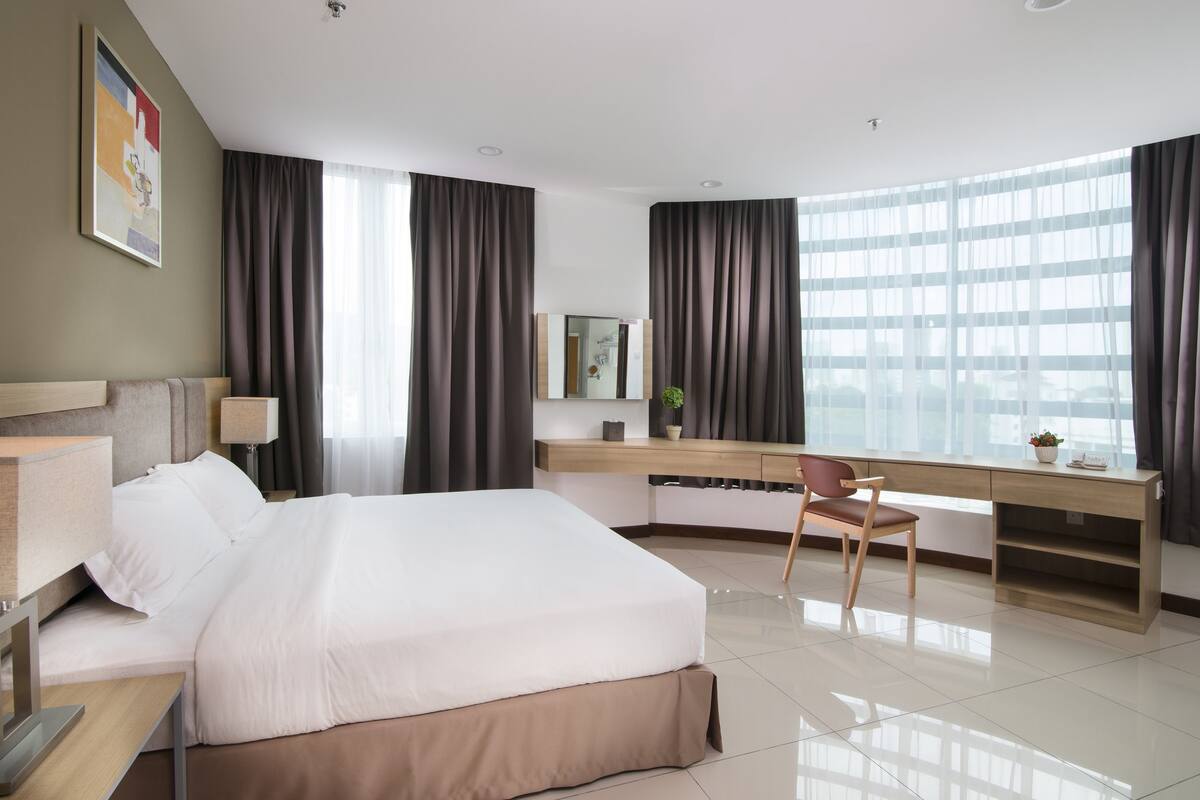 Una habitación de hotel moderna con una cama grande, un escritorio con silla, un espejo y una ventana con cortinas.
