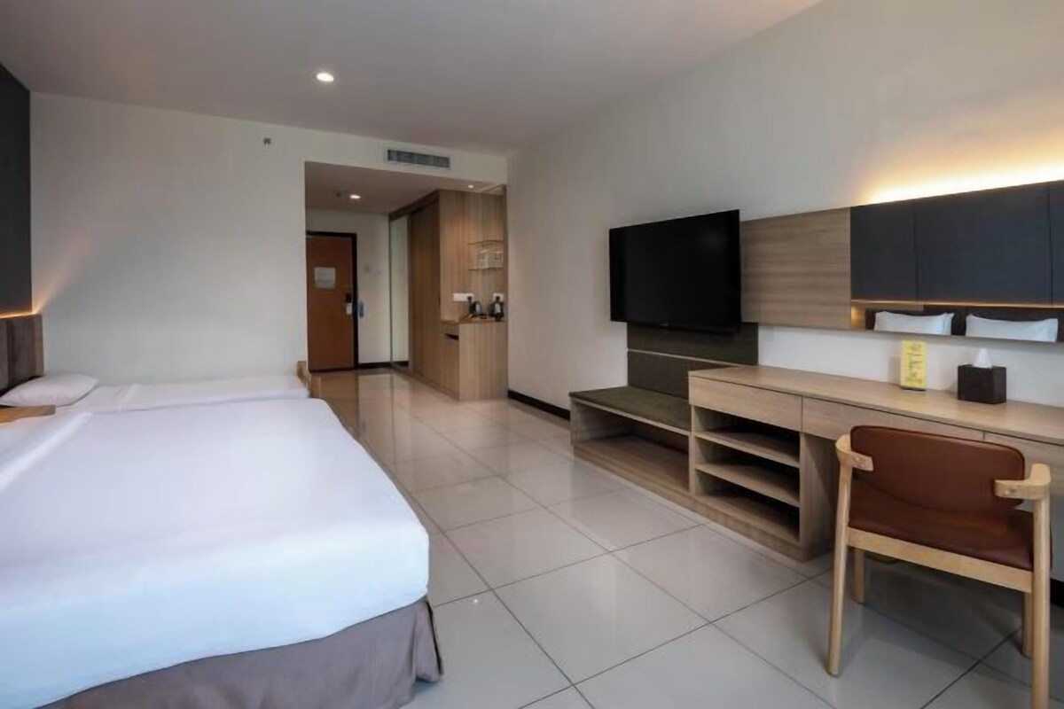 A hotel room with a large bed, a desk with a chair, a television, and a small kitchenette area.