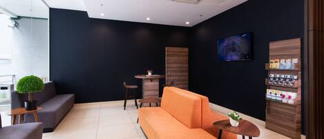 Un vestíbulo moderno con una pared oscura, un mostrador de recepción de madera, un televisor de pantalla plana y una exhibición de artículos de aseo.